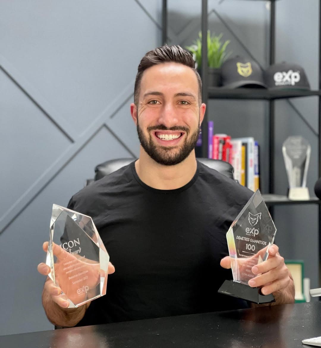 Demetres Giannitsos at his desk, holding two eXp Realty awards.